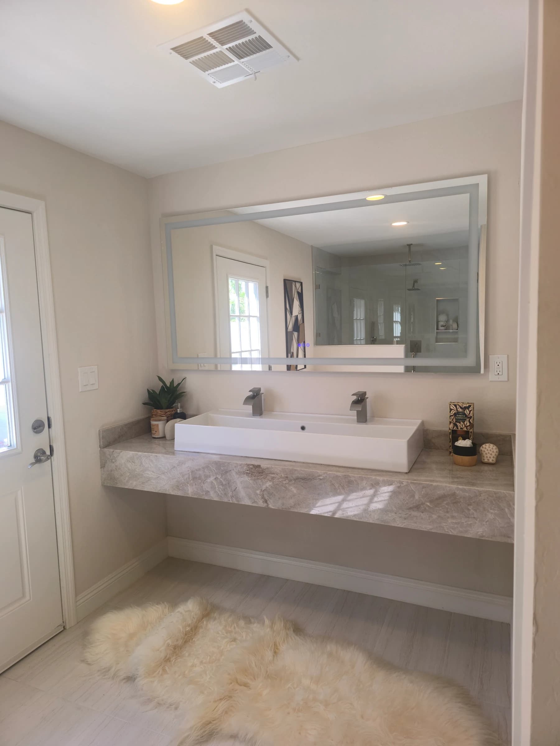 Floating stone vanity with a trough sink and two faucets.