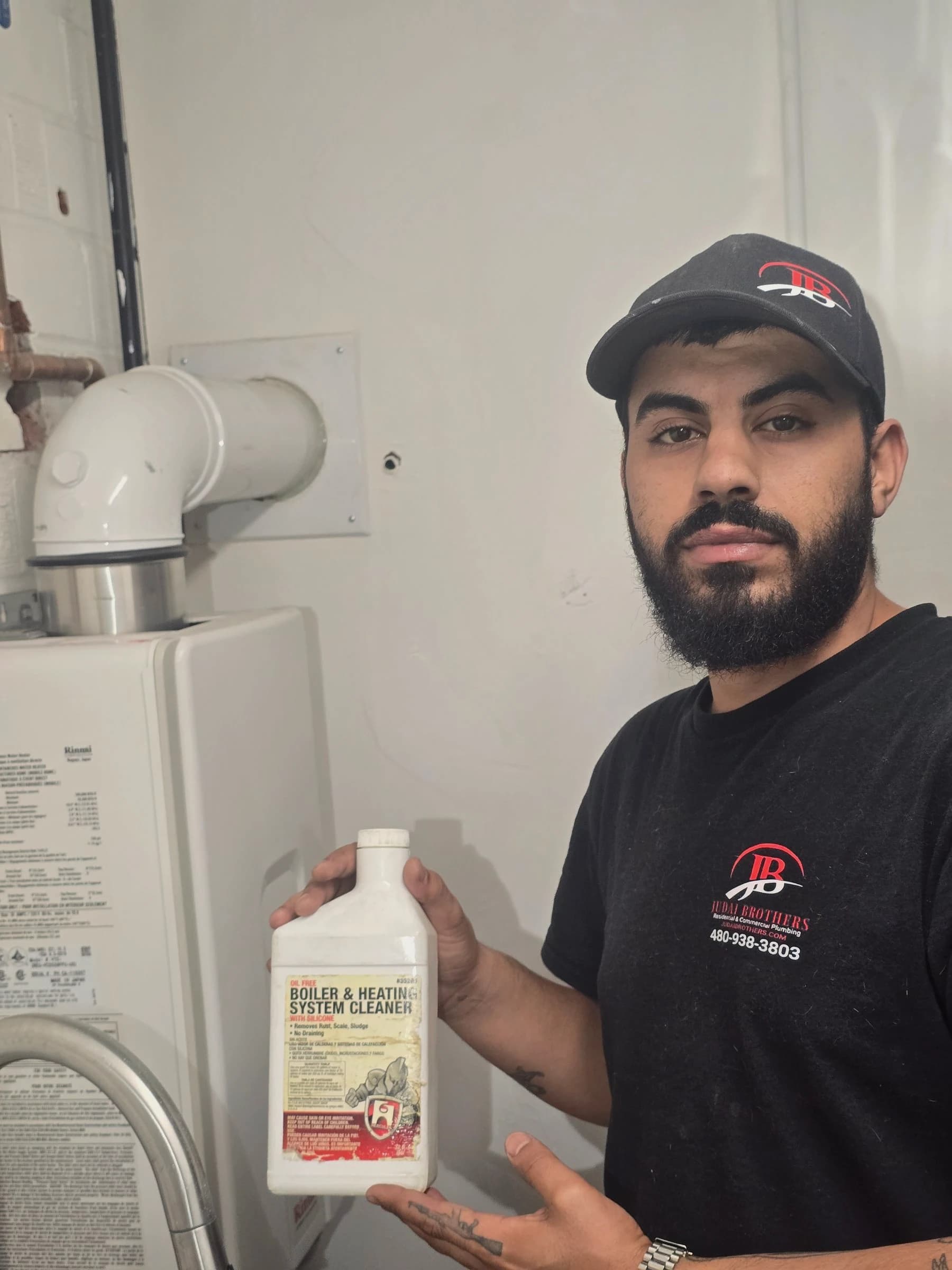 One of the Judai brothers in a branded cap and shirt beside a Rinnai tankless water heater